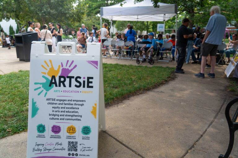 Una imagen de un cartel de ARTSiE frente al acto de inauguración de «Creative Placemaking», con los asistentes de pie al fondo.