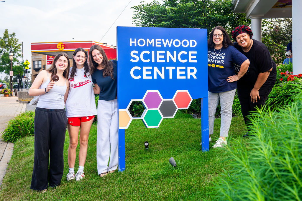 Personas posando junto al cartel del Homewood Science Center, frente al centro.